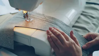 Close-up of a person's hands guiding fabric through a sewing machine, representing skilled craftsmanship and ethical labor.